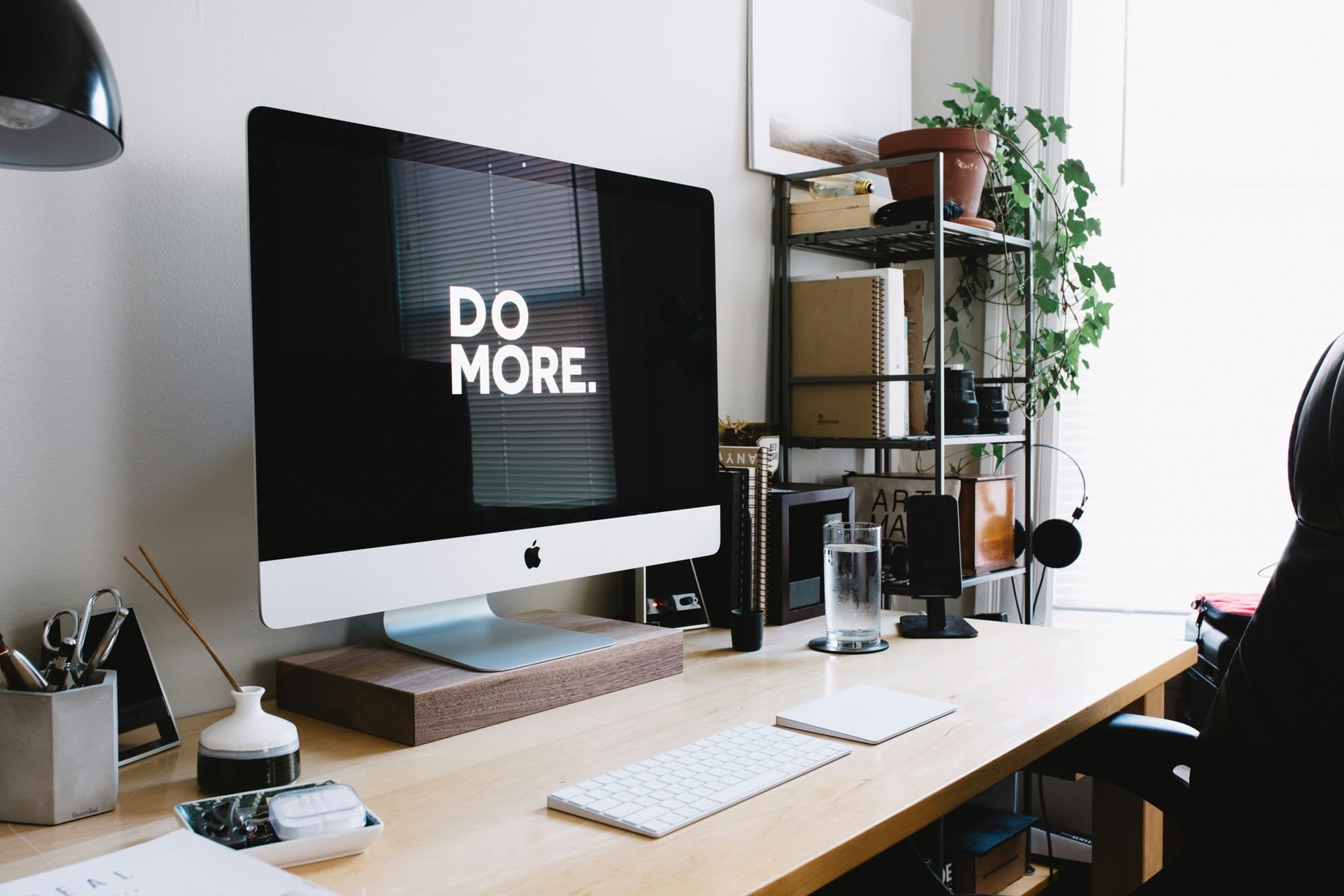 Tidy home office desk with an iMac displaying "Do More", keyboard, plants and shelves