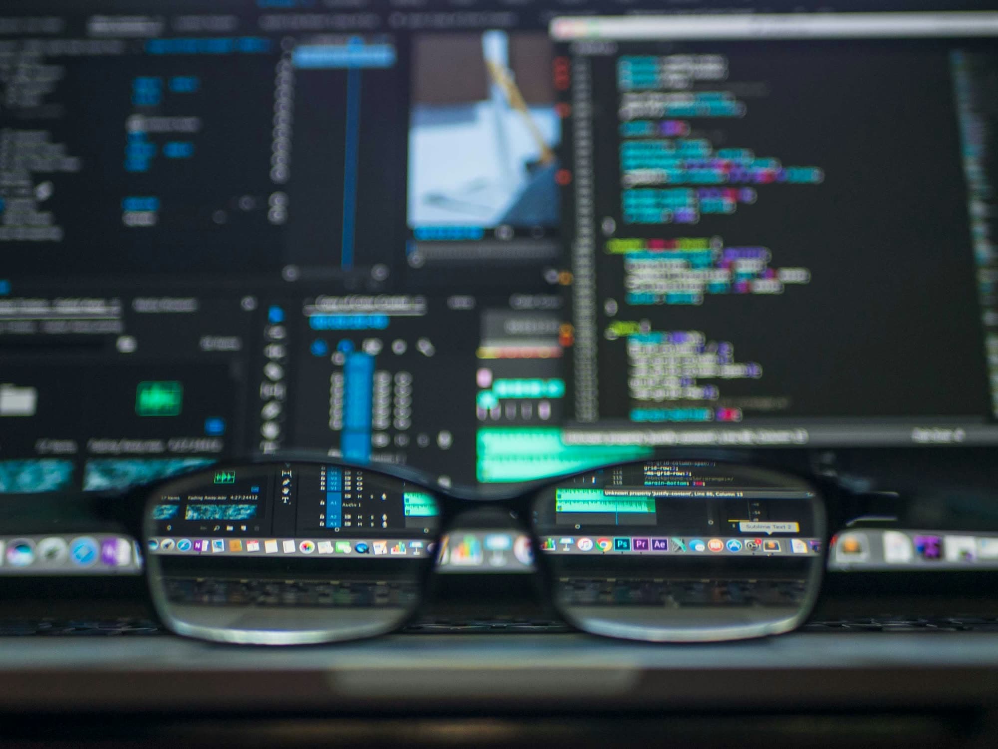 Eyeglasses in front of a computer screen showing code and editing software
